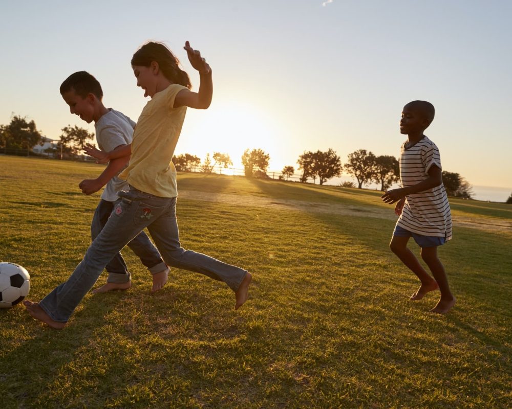 Three children playing football in a field
